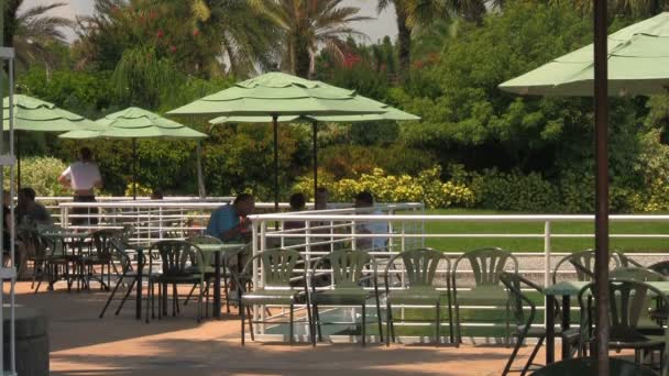 フロリダ州オーランドのシーワールドアドベンチャーパークを訪れる認識できない人々は 暑い夏の日に水辺のテラスで傘の下で昼食をとる — ストック動画