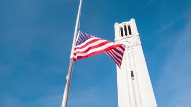 Memorial Bell kule Raleigh Kuzey Carolina NC Devlet Üniversitesi 'nde sallayarak Amerikan bayrağı ile bir mavi gökyüzü arka plan ile düşük açı görüldü