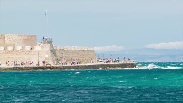 晴れた夏の日に青い地中海に対して歴史的なランドマークに沿って歩くハニアクレタギリシャの観光観光客とオーシャンフロントフォート — ストック動画