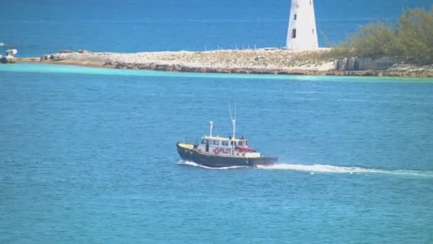 バハマの首都の晴れた日に象徴的な灯台を過ぎて熱帯青い水で港を出るナッソーバハマのパイロットボート — ストック動画