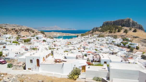 人気のギリシャの島の目的地で晴れた日に背景に考古学アクロポリスサイトを持つ伝統的な白いギリシャの建物をフィーチャーしたロードスギリシャのリンドスの町 — ストック動画