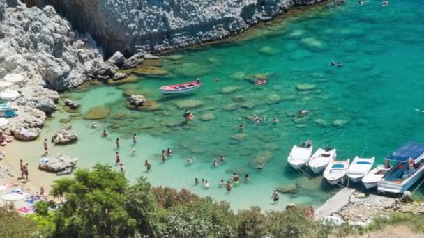 地中海の夏の晴れた日に大きな岩の隣にクリスタルクリアブルー地中海水で泳ぐロードスギリシャのリンドスのセントポールズベイのサンディビーチの人々 — ストック動画