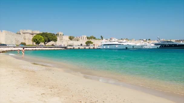 古代旧市街の城壁を背景にアクティサクトゥーリのロードスギリシャビーチと晴れた日にエーゲ海の水を楽しむ観光客 — ストック動画
