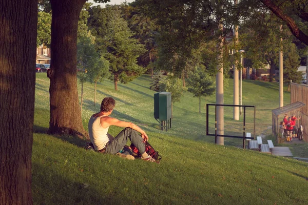 Man watches softball game from beneath a shady tree