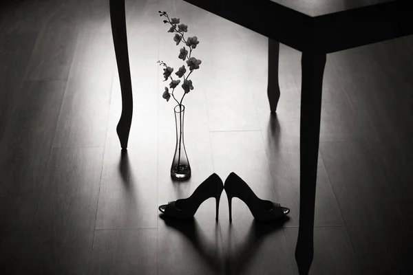 Ein Paar High Heels und eine Blume unter dem Tisch. — Stockfoto