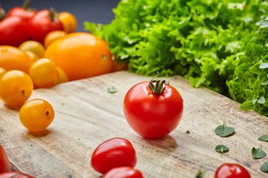 Marul, fesleğen yaprakları ve sarı domates ile çevrili ahşap bir kesme tahtası üzerinde Olgun kiraz domates