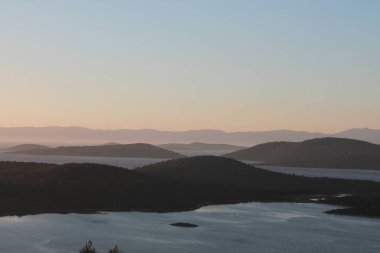 Aydınlatılmış tepeleri olan yüksek dağları olan güzel bir manzara, dağ gölündeki taşlar, yansıma, mavi gökyüzü ve gündoğumunda sarı güneş ışığı.