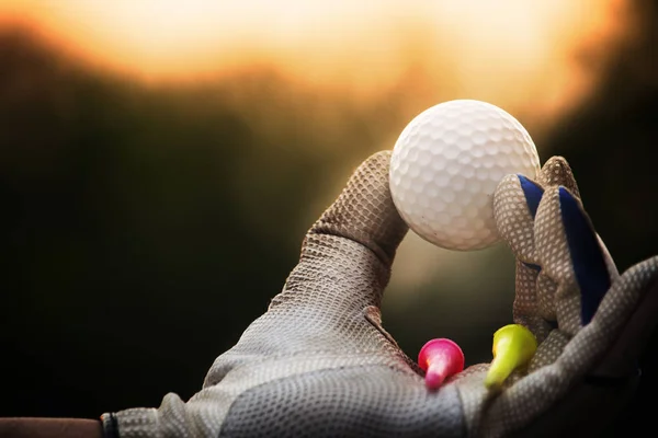 Golf balls and tee in the hands that are worn with white gloves