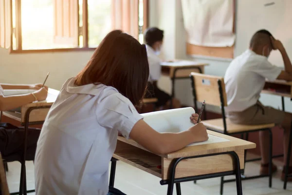 Sınavları üniformalı öğrenciler sınıfta yapıyor. Tahta masaya sınavın cevabını yazmak için elinizi kapayın. Eğitim gelişimi için öğrenme değerlendirmesi
