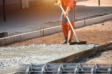 İşçiler beton zemini pürüzsüz hale getirmek için aletler kullanıyorlar. Yol inşaatı veya genel yüzey onarımı