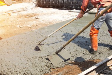 İşçiler beton zemini pürüzsüz hale getirmek için aletler kullanıyorlar. Yol inşaatı veya genel yüzey onarımı