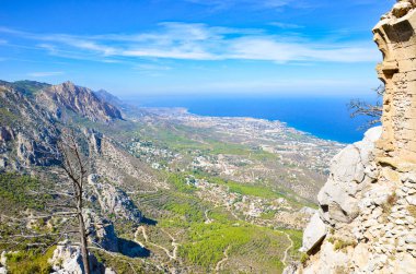 Kuzey Kıbrıs'taki St. Hilarion Kalesi'nin muhteşem manzarası, bitişik dağ sırası ve Akdeniz ile Girne bölgesinin güzel manzarasını sunmaktadır. Yukarıda mavi gökyüzü. Popüler turistik