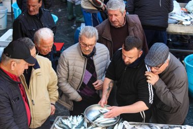Catania, Sicilya, İtalya - Nis 10th 2019: Balıkçı geleneksel bir balık pazarında taze balık satan. Yaşlı adam alıcılar grubu izliyor ve tavsiye veriyor. Popüler yerel cazibe