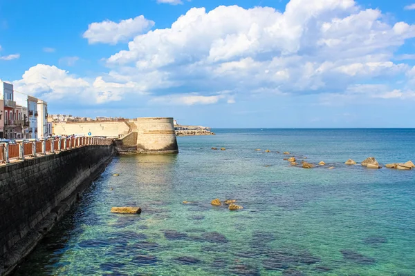 Increíble vista del mar azul y la costa adyacente de la ciudad en Siracusa, Sicilia, Italia en un día soleado con cielo azul. Piedras en el agua de mar. Fotografiado en la isla Ortygia. Lugar turístico popular — Foto de Stock