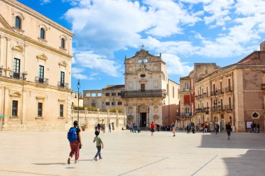 Syracuse, Sicilya, İtalya - Nis 10th 2019: Ortygia Adası Tarihi Piazza Duomo Meydanı güneşli bir günde turistlerle fotoğraflandı. Santa Lucia Kilisesi arka planda. Ünlü turistik yer