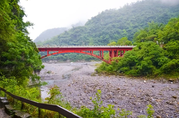 Vista del puente rojo sobre el río en el Parque Nacional Taroko, Taiwán. Garganta del Taroko rodeada de bosque tropical verde y rocas. Fotografiado en niebla brumosa. Clima lluvioso — Foto de Stock