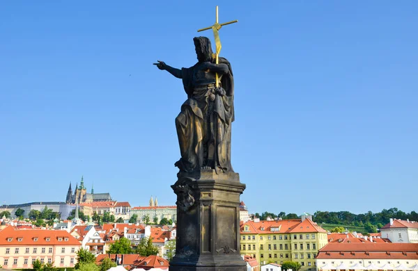 Estatua religiosa en el borde del famoso Puente de Carlos en Praga, República Checa. Castillo de Praga y casco antiguo histórico en el fondo. Cielo azul. Praga, Chequia. Hermosas ciudades. Paisaje urbano — Foto de Stock