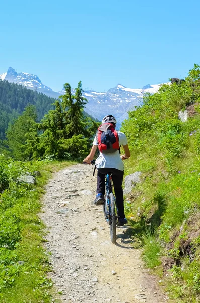 Young man riding bike up to the hill in beautiful Swiss Alps, close to famous Zermatt. Mountain ridges with snow on tops in background. Amazing Switzerland, beautiful nature, outdoor sports. Alpine