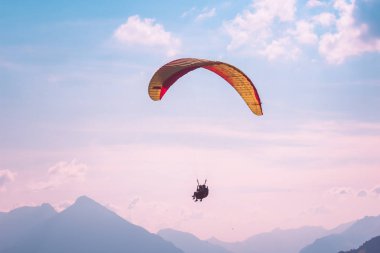 Interlaken, İsviçre'de tandem yamaç paraşütü. Pembe gün batımı ışığında fotoğraflandı. Yamaç paraşütü ve İsviçre Alpleri siluetleri. Macera yaşam tarzı. Ekstrem sporlar. Adrenalin aktivitesi