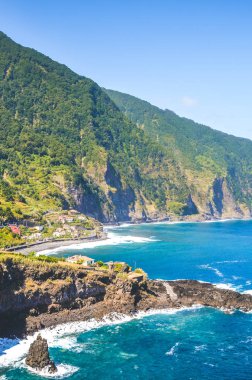 Portekiz 'in Madeira Adası' ndaki Seixal köyünün Atlantik Okyanusu kıyısındaki güzel uçurumlar. Dik yeşil kayalar, küçük şehir ve mavi deniz suyu dikey fotoğrafçılıkla çekildi. Turizm beldesi