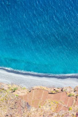 Mavi Atlantik Okyanusu 'nun yanındaki hava manzarası. Portekiz 'in Madeira Adası' nın güney kıyısındaki taş plajı ve bitişik tarlalar. Hava manzarası, inanılmaz doğa. Dikey bir fotoğraftaki yaz titreşimleri