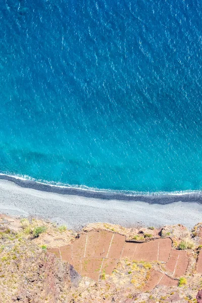 Mavi Atlantik Okyanusu 'nun yanındaki hava manzarası. Portekiz 'in Madeira Adası' nın güney kıyısındaki taş plajı ve bitişik tarlalar. Hava manzarası, inanılmaz doğa. Dikey bir fotoğraftaki yaz titreşimleri