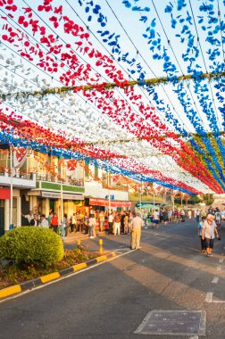 Loreto, Madeira, Portekiz - Sep 7 2019: Dini festival sırasında geleneksel renkli sokak dekorasyonu. Havada asılı kağıt çiçekler. İnsanlar kutluyor, yiyeceklerle ayakta duruyorlar.