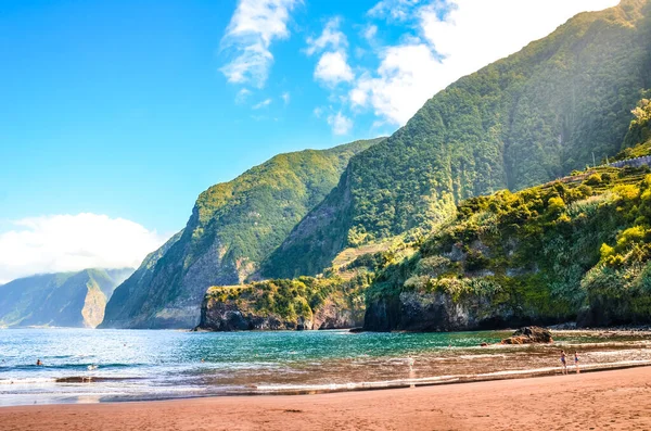 Seixal, Madeira Adası, Portekiz 'deki güzel kumlu plaj. Arka planda tropikal ormanlarla kaplı yeşil tepeler. Sahildeki insanlar. Yaz tatilinde. Portekiz manzarası
