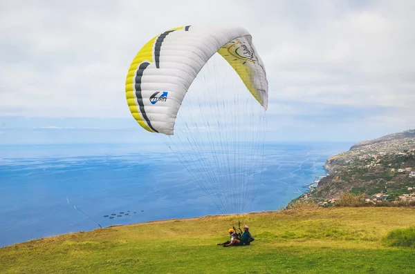 Arco da Calheta, Madeira, Portugal - Sep 16, 2019: Tandem paragliders που προσγειώνονται σε ένα γρασίδι στα βράχια πάνω από τον Ατλαντικό ωκεανό. Μαντείρα τοπίο στο παρασκήνιο. Αλεξίπτωτο, ενεργές διακοπές — Φωτογραφία Αρχείου