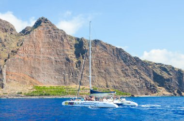 Madeira, Portekiz - 10 Eylül 2019: Atlantik Okyanusu 'nun sularında insanlarla birlikte turistik gezi teknesi. Arka planda Madeira Adası 'ndaki kayalar. Balina izliyor, yunus gezileri izliyor.