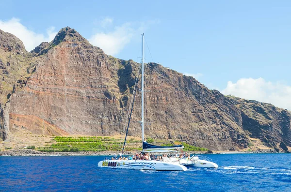 Madeira, Portekiz - 10 Eylül 2019: Atlantik Okyanusu 'nun sularında insanlarla birlikte turistik gezi teknesi. Arka planda Madeira Adası 'ndaki kayalar. Balina izliyor, yunus gezileri izliyor.