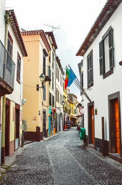 Funchal, Madeira, Portugal - 21 sep 2019: En kullerstenssmal gata i Madeiras gamla stad med mulen himmel. Historiska byggnader med portugisisk och europeisk flagg. Stadens centrum — Stockfoto