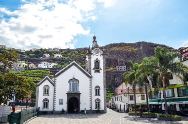 Ribeira Brava, Madeira, Portekiz - 9 Eylül 2019: Şehir merkezindeki güzel Roma Katolik Kilisesi. Meydanda palmiye ağaçları. Arka planda kayalık bir tepede muz tarlaları