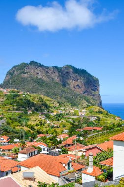 Portekiz 'in Madeira adasındaki Porto da Cruz köyü. Yeşil tepelerdeki evler, kaya oluşumu, arka planda Atlantik Okyanusu kıyısındaki uçurum. Tepe arazisi. Portekiz manzaraları
