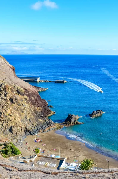Ciemnopiaszczysta plaża Prainha nad Oceanem Atlantyckim na Maderze, Portugalia. Otoczony wulkanicznymi skałami i klifami. Ludzie na plaży, słoneczny dzień. Tłumaczenie znaków: Prainha - mała plaża w języku portugalskim — Zdjęcie stockowe