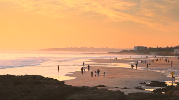 Movimento lento das pessoas na praia de Carcavelos durante o pôr-do-sol amarelo profundo, Portugal — Vídeo de Stock