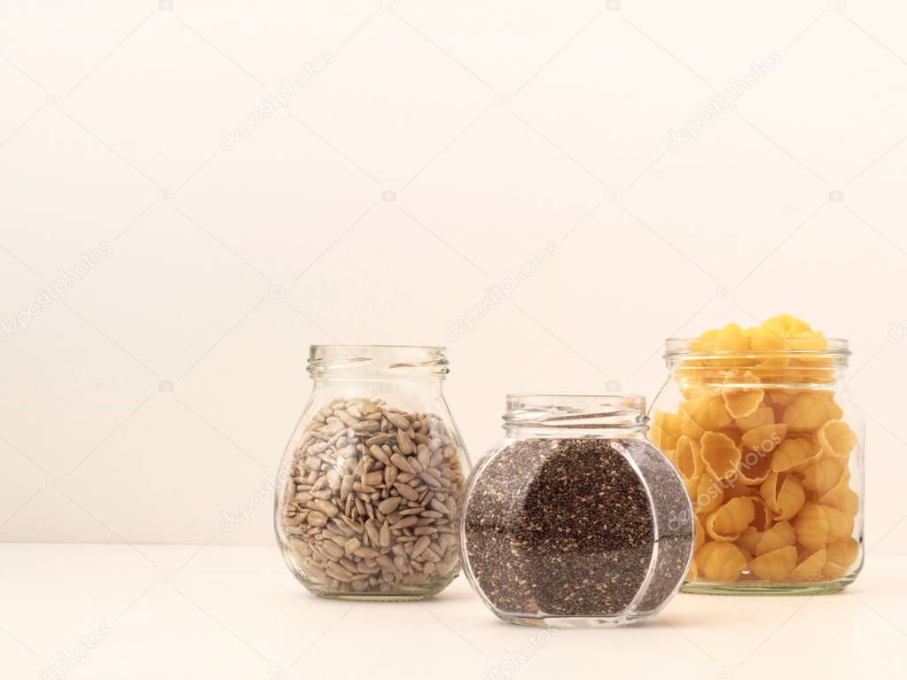 Three recycled jars used to store dried goods, namely pasta, chia seeds and sunflower seeds. Concept of recycling and zero-waste lifestyle.