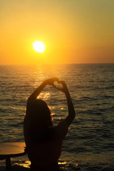 Silhouette of a girl on a sunset background that holds heart sha — Stock Photo, Image