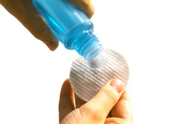Kız beyaz arka planda izole edilmiş makyajı temizlemek için kozmetik bir süngerin üzerine su döküyor. Güzellik konsepti.
