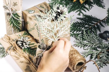 Çocuk, Noel ağacı dalları ve koni ile el yapımı Noel hediyelerini el yapımı kağıda sarıp yeni yıl kutlaması için hediyeler hazırlıyor. Kış tatilinden önce huzurlu eğlence aktiviteleri