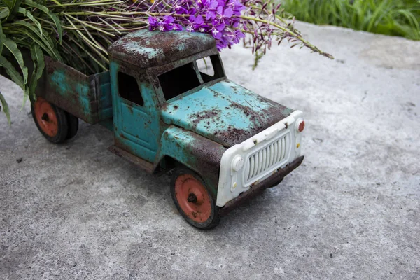 toy metal machine with traces of corrosion. Rust on the machine\'s gland. Flowers of fireweed by car.