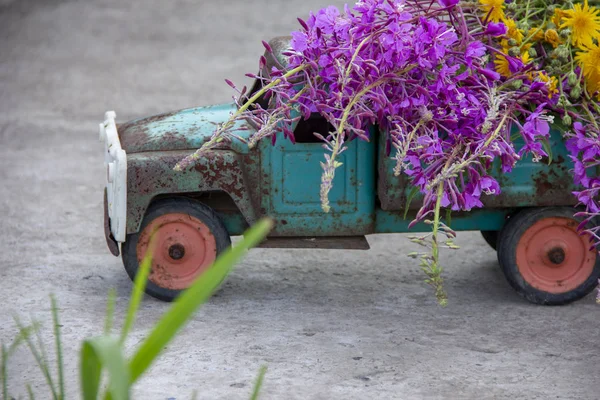 toy metal machine with traces of corrosion. Rust on the machine\'s gland. Flowers of fireweed by car.