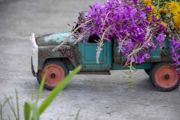 toy metal machine with traces of corrosion. Rust on the machine's gland. Flowers of fireweed by car.