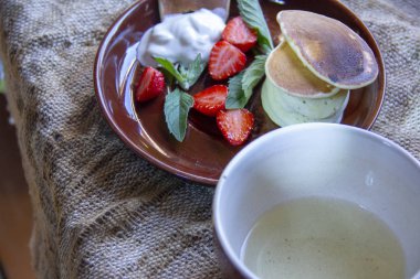 harika bir kahvaltı. Doğranmış çilek ve nane yaprakları ile tabaklarda Börek. Bir tabak ve bir fincan çay jüt peçete üzerinde.