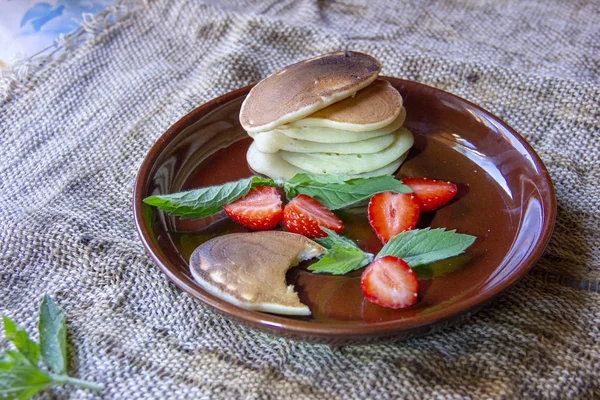 Bon petit déjeuner. Beignets sur assiettes avec fraises hachées et feuilles de menthe. Une assiette et une tasse de thé sont sur une serviette de jute . — Photo