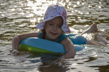 küçük kız bir panama ve bir mayo nehir suyunda bir lastik halka üzerinde yüzer