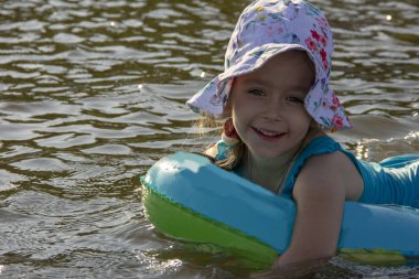 küçük kız bir panama ve bir mayo nehir suyunda bir lastik halka üzerinde yüzer
