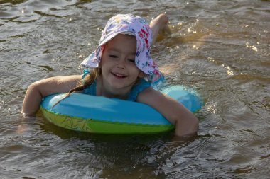 küçük kız bir panama ve bir mayo nehir suyunda bir lastik halka üzerinde yüzer