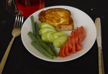 çırpılmış bir yumurta kızartılmış tost doğranmış domates, salatalık ve yeşil soğan ile beyaz bir tabak üzerinde yatıyor. Harika bir kahvaltı. siyah bir masa örtüsü üzerinde yemekleri hizmet