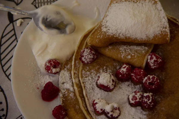 Pancakes on a plate with raspberries and sprinkled with powdered sugar. Holiday - Shrovetide. round treat — Stock Photo, Image